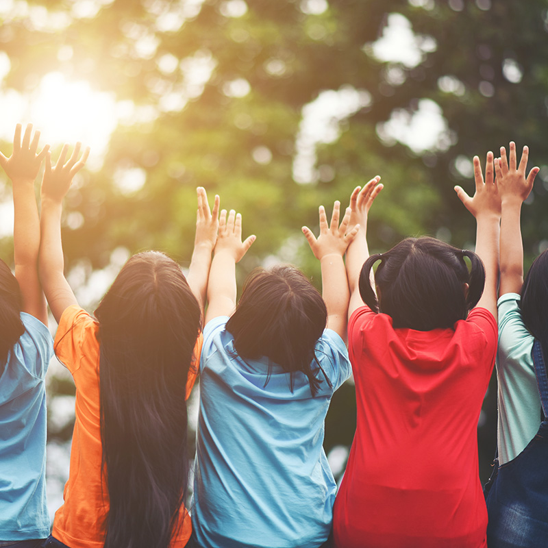 Group of kids with arms in the air toward the sun