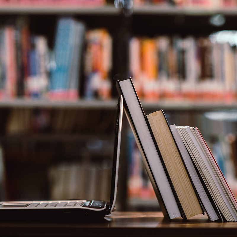 Books leaning up against a laptop on a desk in a library