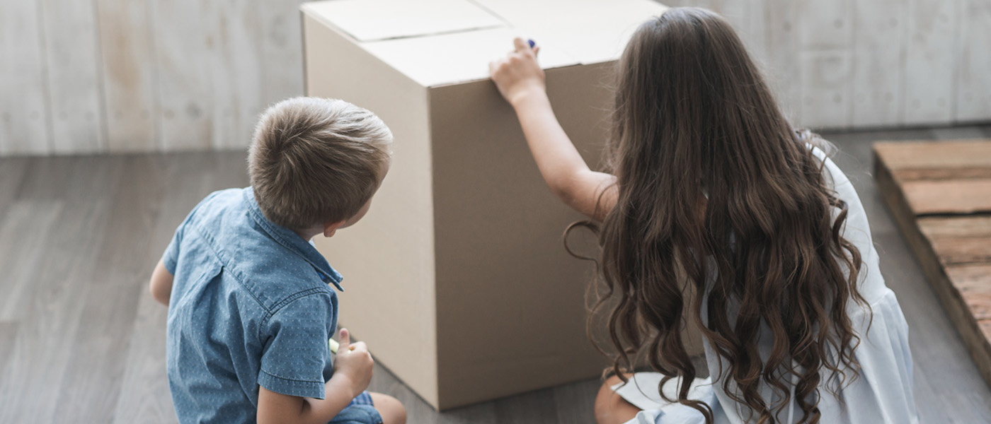 Two children sitting on the floor and drawing on a cardboard box