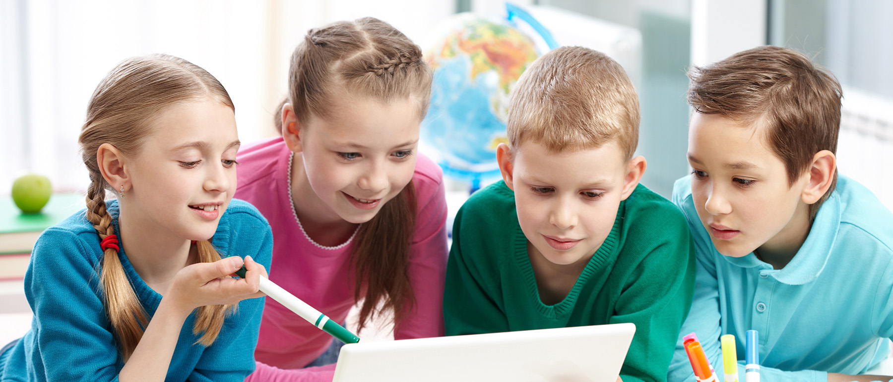 Portrait of smart schoolgirls and schoolboys looking at the laptop in classroom