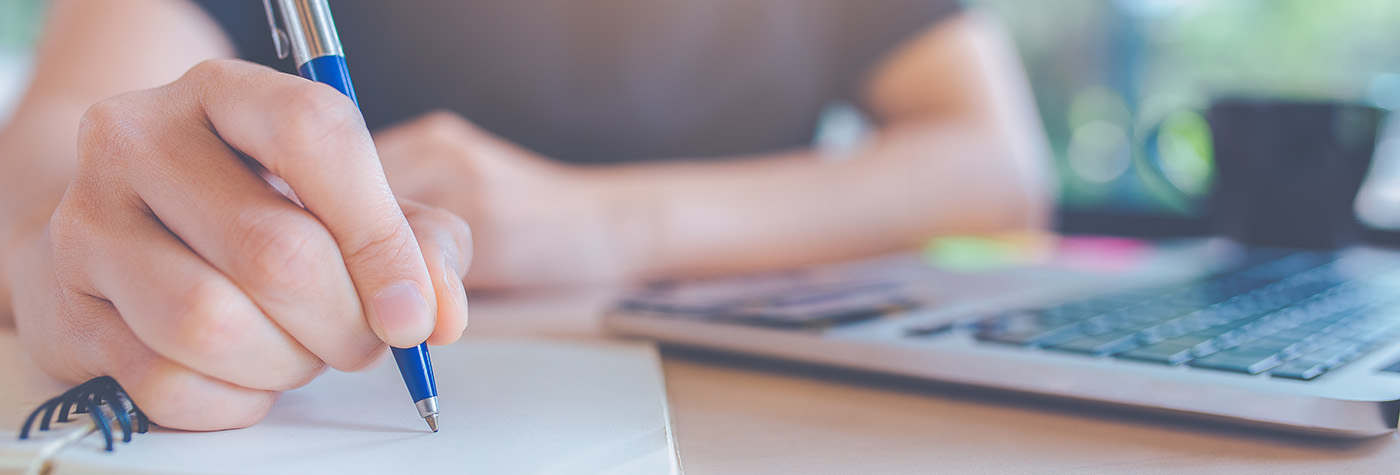 Woman hand is writing on a notepad with a pen in office