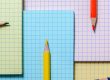 Colored pencils lie on the background of multi-colored notebook sheets. Checkered sheets and color pencils. The concept of elementary and high school.