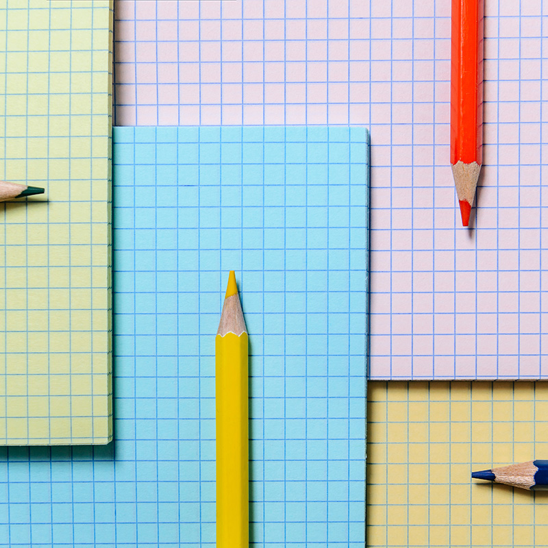 Colored pencils lie on the background of multi-colored notebook Colored pencils lie on the background of multi-colored notebook sheets. Checkered sheets and color pencils. The concept of elementary and high school.