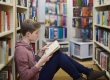 Boy taking a reading break in between library book shelves
