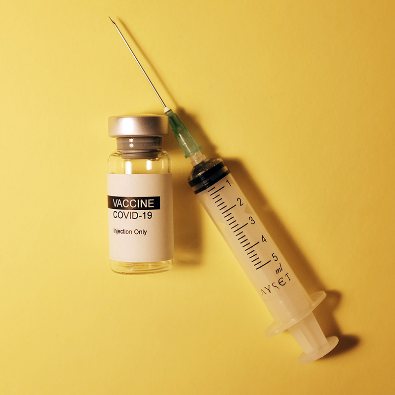 COVID vaccination ampule and syringe on yellow background