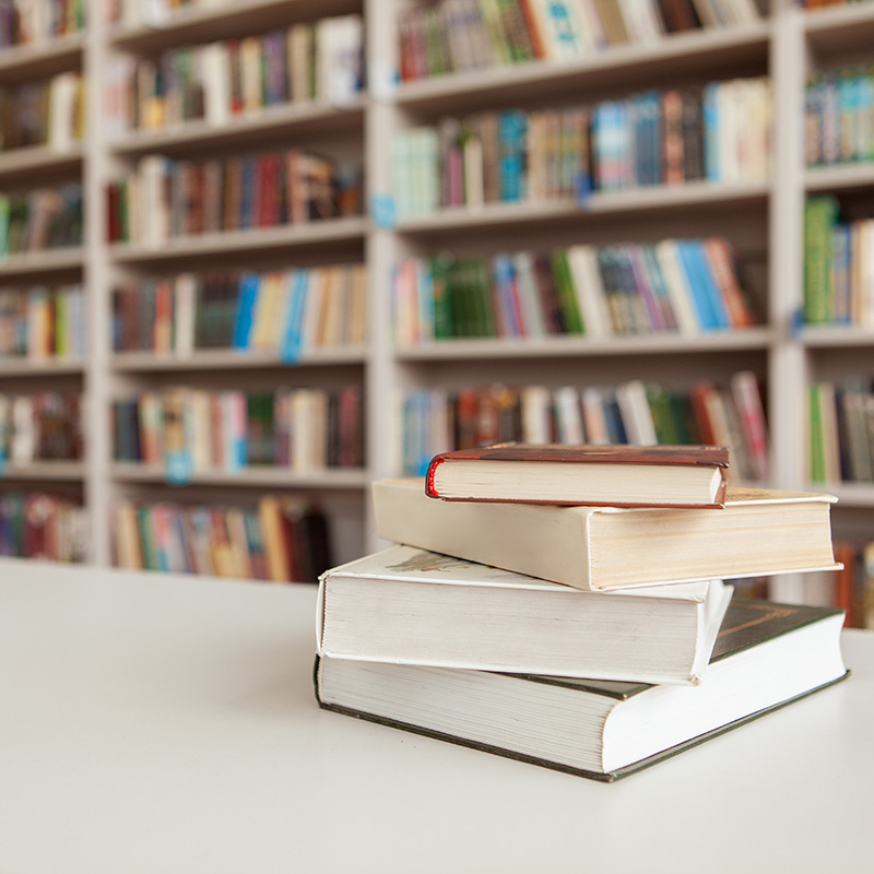 Pile of books on the table at college library, stacked bookshelves on background. Book stack at library room