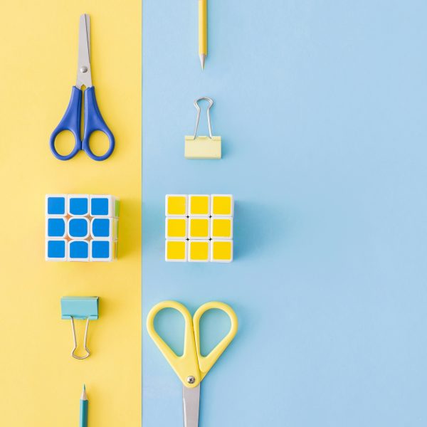 Rubik's and scissors on a colourful blue and yellow paper background