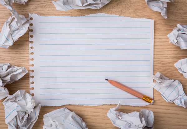 White note book paper with pencil and crumpled paper on a wood