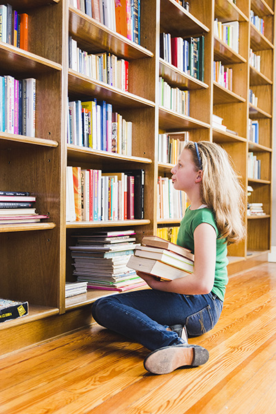 Girl sitting holding books and looking at bookshelf full of books