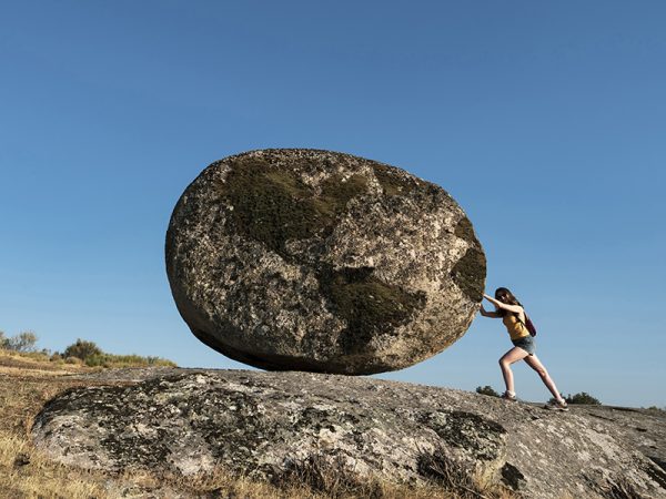 Woman pushing a world rock. Metaphor for the effort of working w Woman pushing a world rock. Metaphor for the effort of working