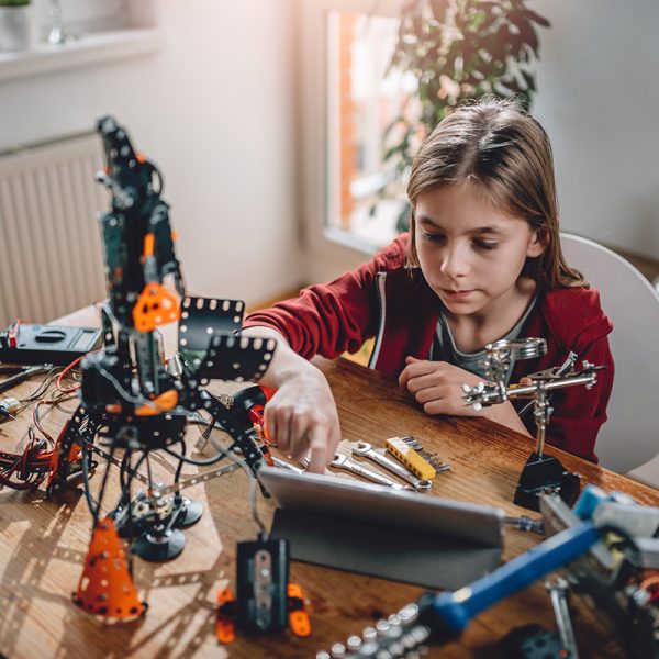 Girl wearing red hoodie building a robot at home and using digital tablet