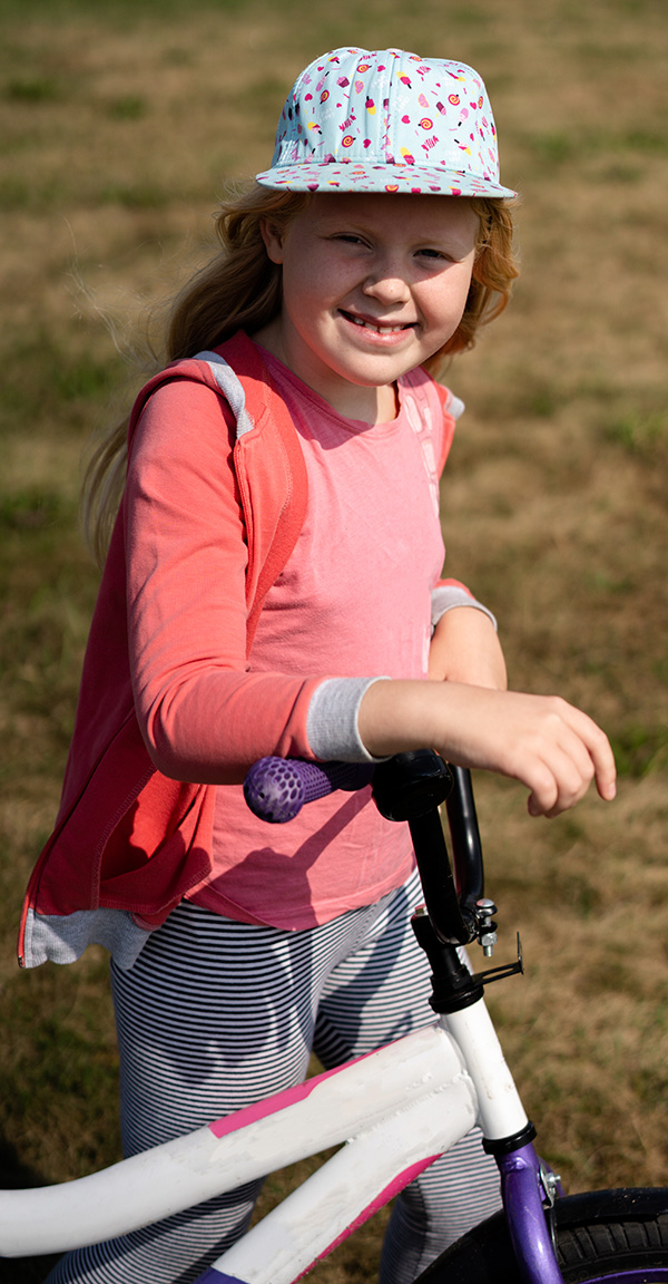 Red haired girl wearing hat stands next to bicycle