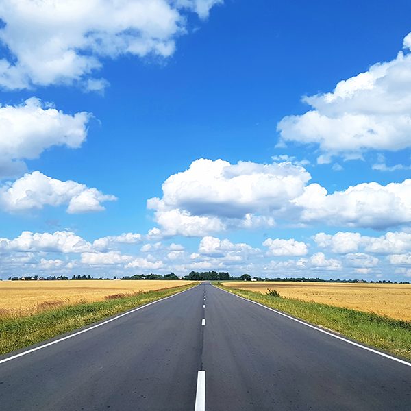 View of the asphalt highway which is in a field with wheat against the blue sky with white clouds. Concept landscape, background.