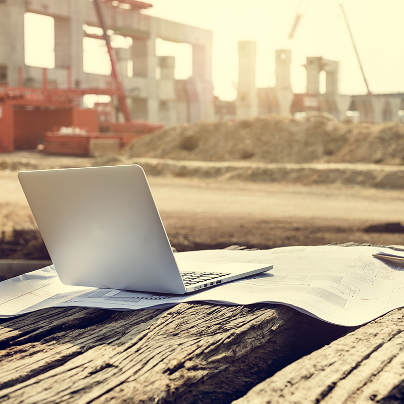 Laptop in foreground on a wooden table overlooking a construction site