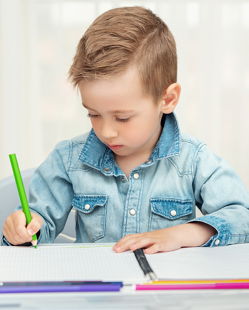 Boy wiriting with green pen on a notepad