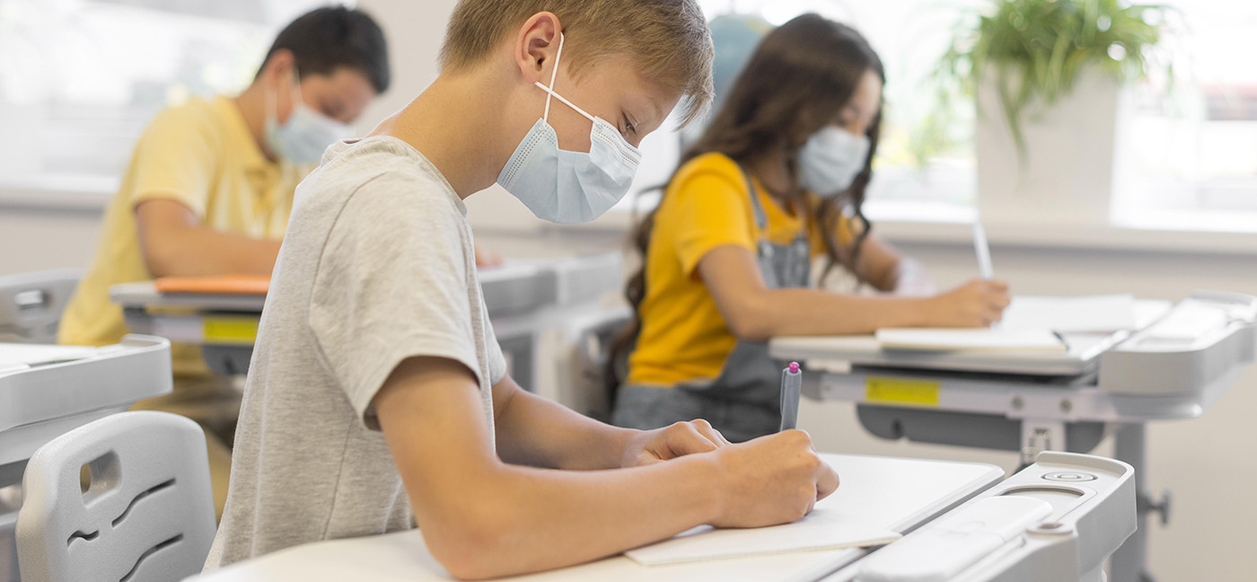 Young children in masks writing at desks in classroom