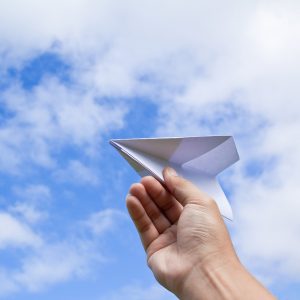 plane in hand hand with paper plane against blue sky with clouds