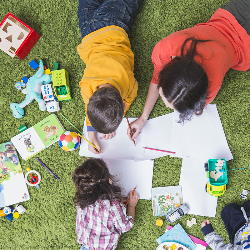 Children drawing and playing on the carpet shown from above