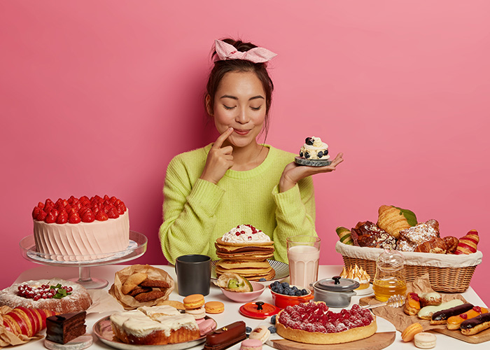 Pleased brunette woman holds small creamy muffin, bakes many desserts for New Year holiday or festive time, demonstrates her culinary abilities, has special occasion, degustates homemade cupcake