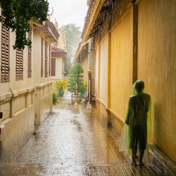 PHNOM PENH, CAMBODIA - Aug 06, 2017: Asian teen wearing a transparent green rain jacket, waiting for the heavy monsoon rain to stop during a heavy rain shower in Phnom Penh city, Cambodia