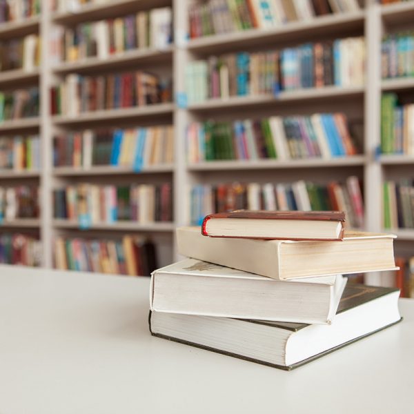 Pile of books on the table at college library, stacked bookshelves on background. Book stack at library room
