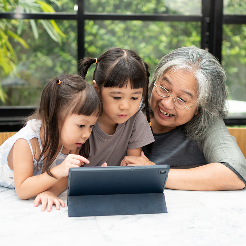 Asian Grandmother with her two grandchildren having fun and playing education games online with a digital tablet at home in the living room. Concept of online education and caring from parents.
