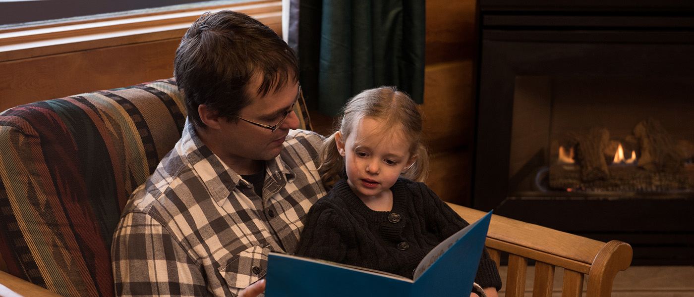 Father reading story book to daughter on chair at home