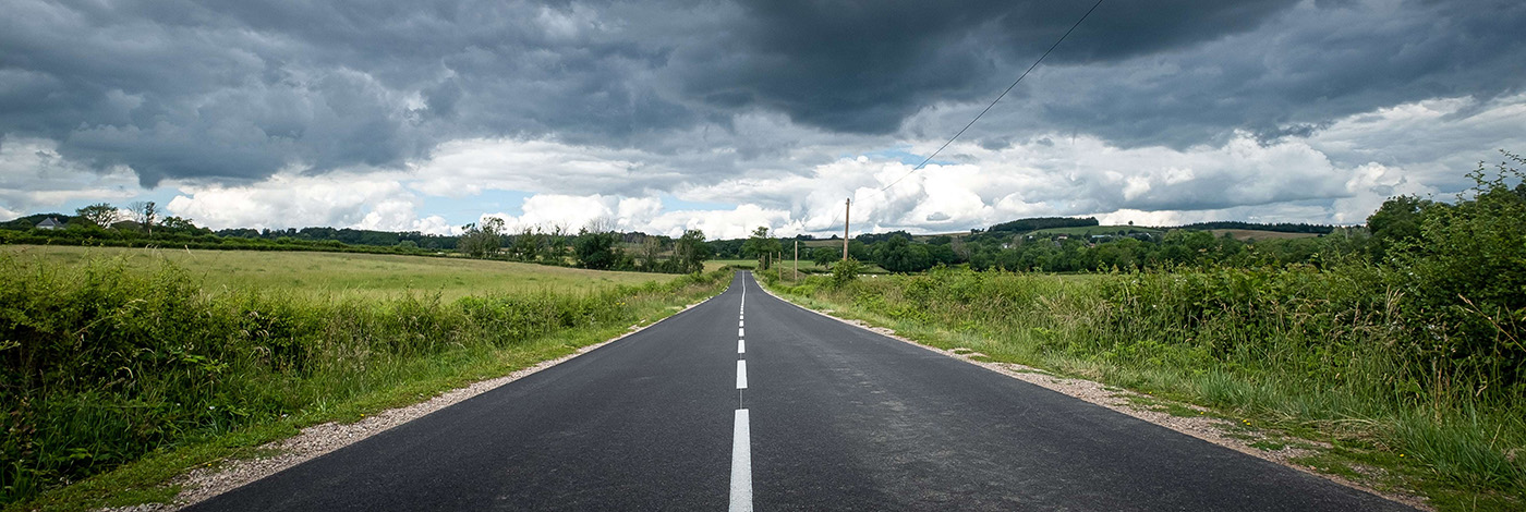 A beautiful view of an empty road surrounded by greenery under dark storm clouds