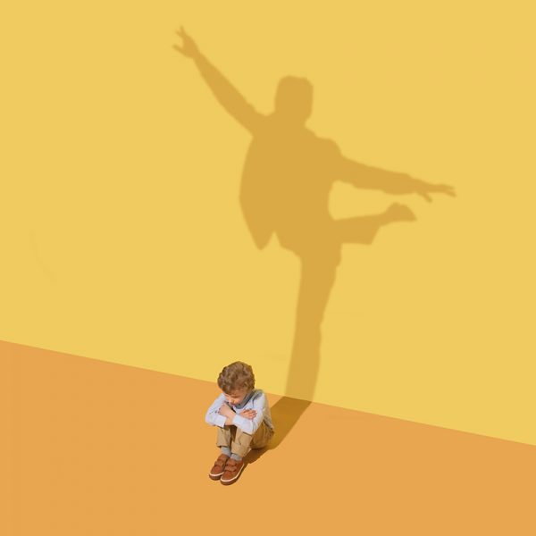Flexibility. Childhood and dream concept. Conceptual image with child and shadow on the yellow studio wall. Little boy want to become ballet dancer, artist in theatre or businessman, office man.