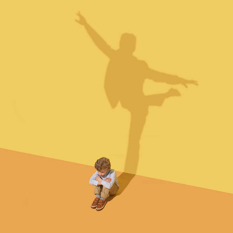 Flexibility. Childhood and dream concept. Conceptual image with child and shadow on the yellow studio wall. Little boy want to become ballet dancer, artist in theatre or businessman, office man.